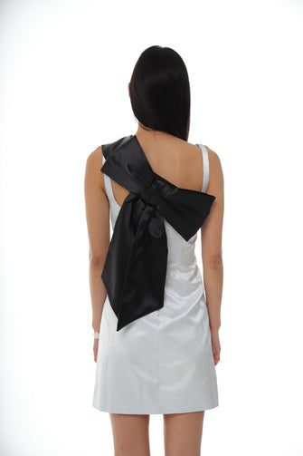A woman wears a blue satin dress with a black adjustable sash bag with a bow design, displayed against a plain background.