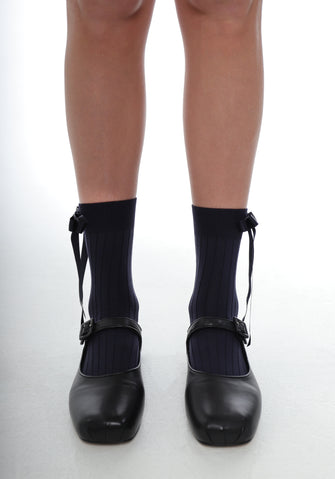 A pair of navy crew socks with a ribbon bow on the side, worn with black shoes.