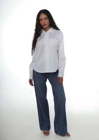 Woman wearing a white button down shirt featuring a peter pan collar paired with blue jeans with rhinestone details along the side and sandals