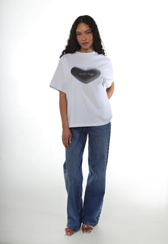A woman wears a white tshirt with heart shaped graphic printed on with a pair of blue jeans against a white background
