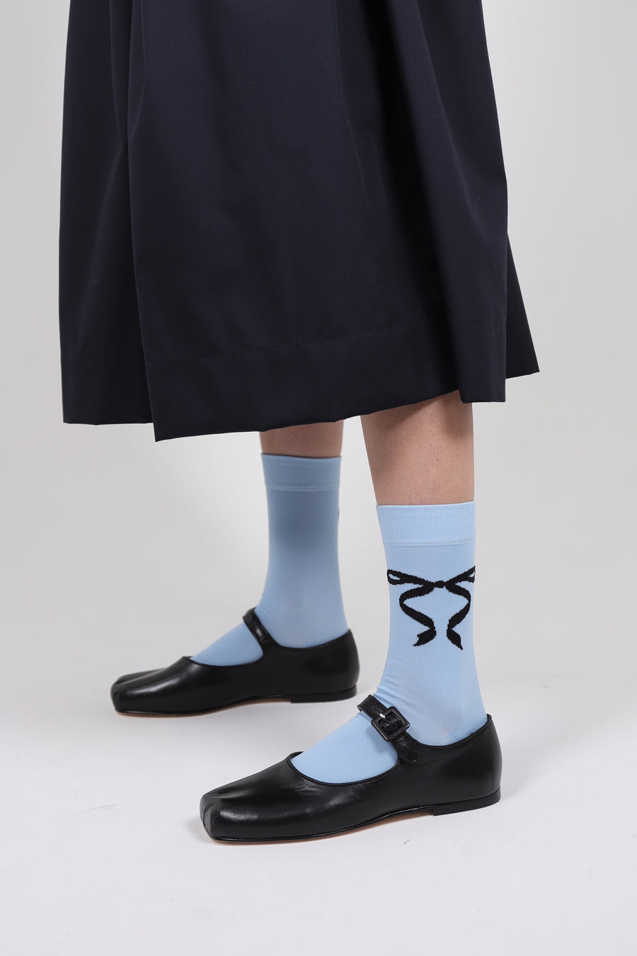 Baby blue crew length socks with black bows on either sides on model